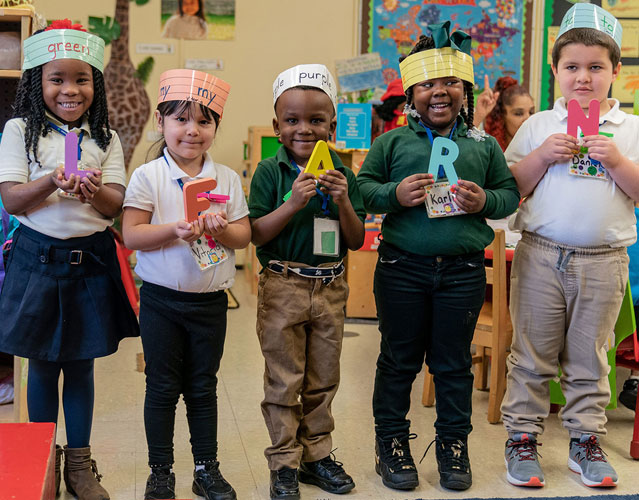 Preschool students standing, holding letters that spell the word, learn.